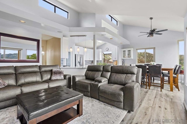 living room featuring ceiling fan, a towering ceiling, and light hardwood / wood-style flooring