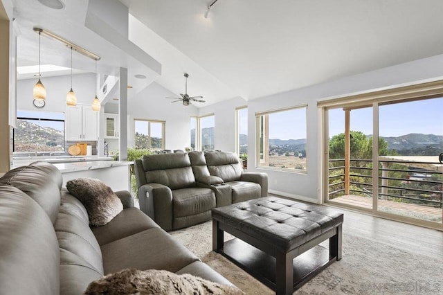 living room with ceiling fan, vaulted ceiling, a mountain view, and light hardwood / wood-style flooring