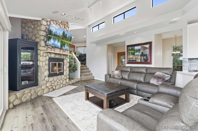 living room with an inviting chandelier, track lighting, light hardwood / wood-style flooring, and a stone fireplace