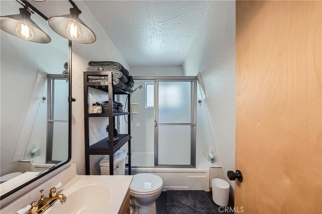 full bathroom with a textured ceiling, combined bath / shower with glass door, vanity, and toilet