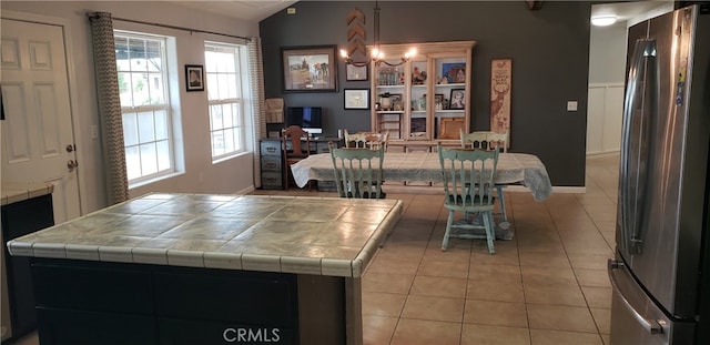 kitchen featuring lofted ceiling, tile countertops, light tile patterned floors, and stainless steel fridge