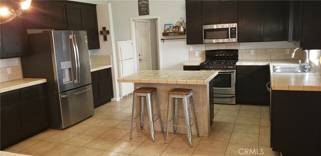 kitchen featuring appliances with stainless steel finishes, backsplash, tile countertops, a center island, and sink