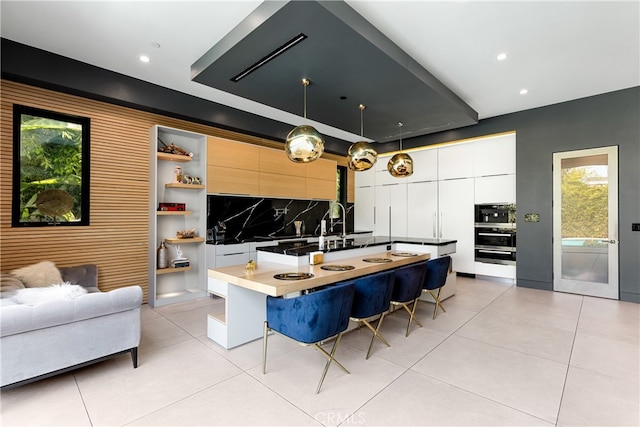 kitchen featuring white cabinetry, decorative backsplash, a kitchen breakfast bar, a center island with sink, and decorative light fixtures