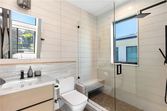 bathroom with vanity, backsplash, a shower with shower door, tile walls, and toilet