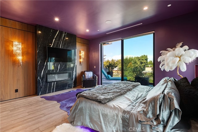 bedroom featuring light wood-type flooring, wood walls, a high end fireplace, and access to exterior