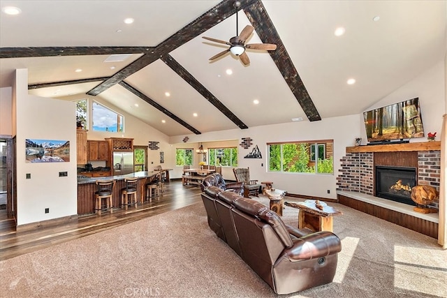 living room with high vaulted ceiling, a brick fireplace, wood-type flooring, beam ceiling, and ceiling fan