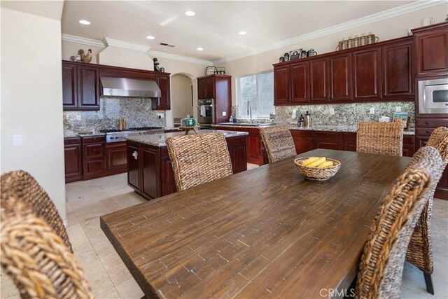 kitchen featuring ornamental molding, wall chimney exhaust hood, appliances with stainless steel finishes, a center island, and light stone countertops