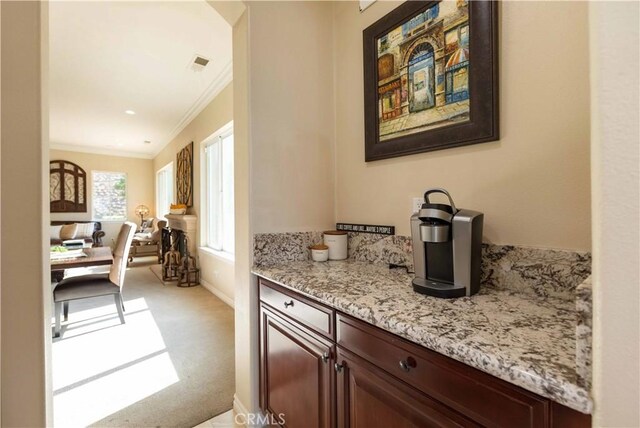 bar featuring dark brown cabinets, ornamental molding, light stone counters, and light carpet