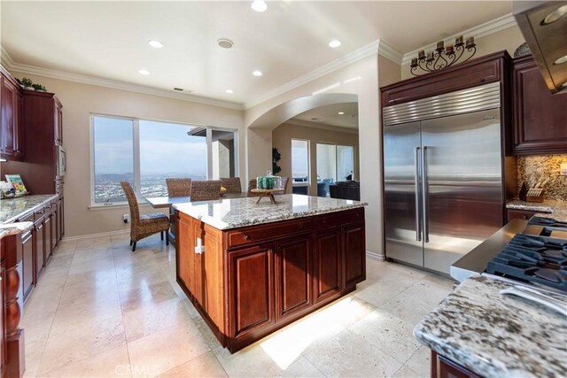 kitchen featuring stainless steel built in fridge, light stone countertops, a kitchen island, crown molding, and backsplash