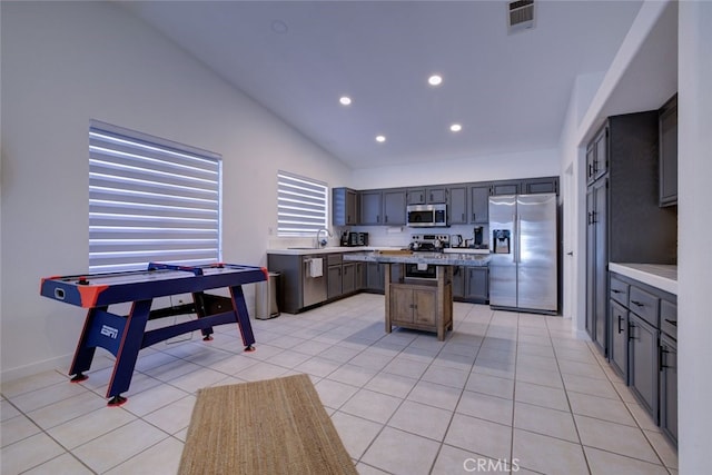 kitchen with appliances with stainless steel finishes, lofted ceiling, a kitchen island, and light tile patterned floors