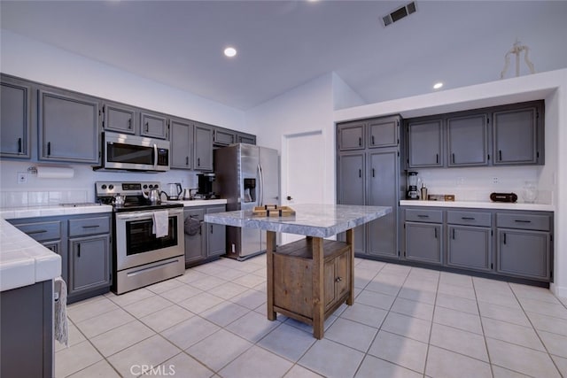 kitchen featuring lofted ceiling, gray cabinetry, stainless steel appliances, tile countertops, and light tile patterned floors