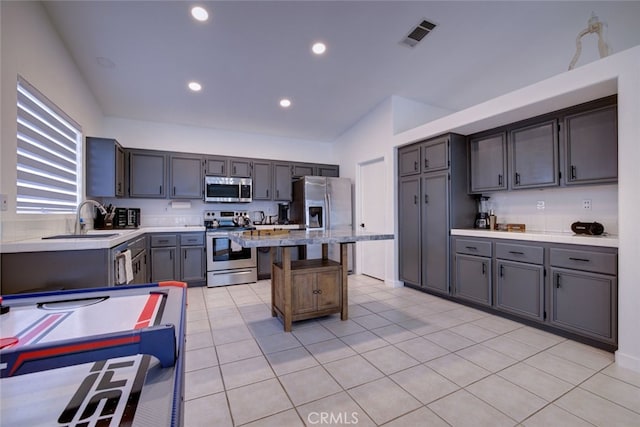 kitchen with light tile patterned floors, sink, gray cabinetry, stainless steel appliances, and vaulted ceiling