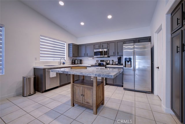 kitchen featuring vaulted ceiling, a kitchen bar, a kitchen island, stainless steel appliances, and light tile patterned floors