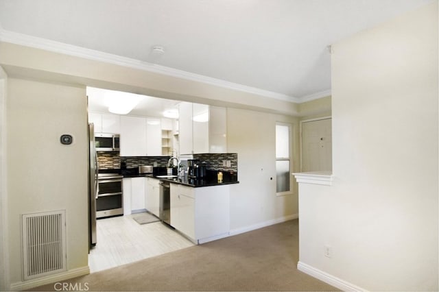 kitchen with white cabinets, backsplash, stainless steel appliances, crown molding, and light carpet