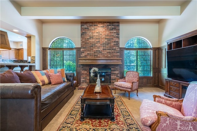 living room with beam ceiling, a brick fireplace, a towering ceiling, and light colored carpet