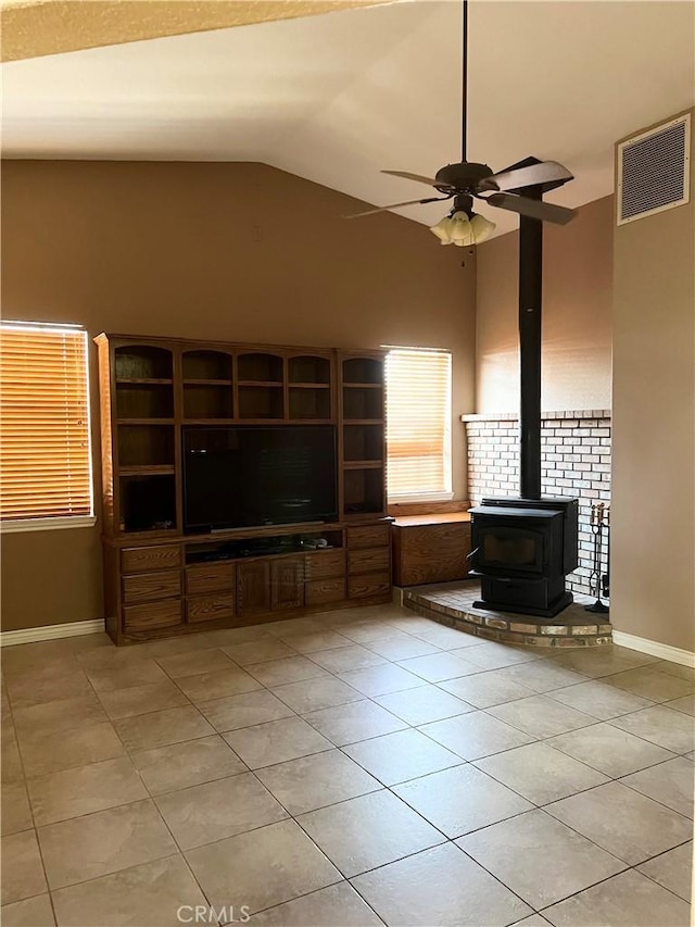 unfurnished living room with visible vents, a ceiling fan, a wood stove, vaulted ceiling, and light tile patterned flooring