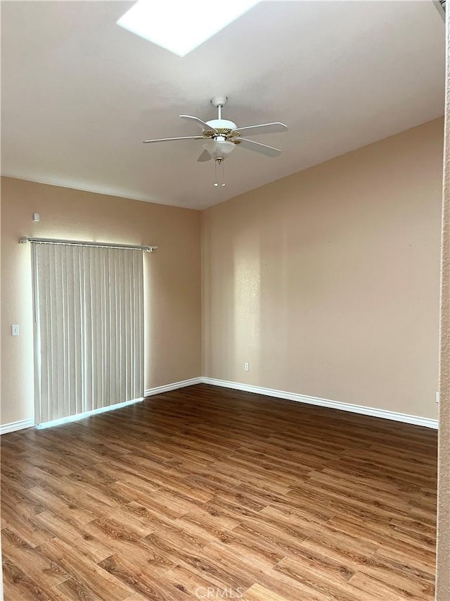 unfurnished room featuring a ceiling fan, a skylight, baseboards, and wood finished floors