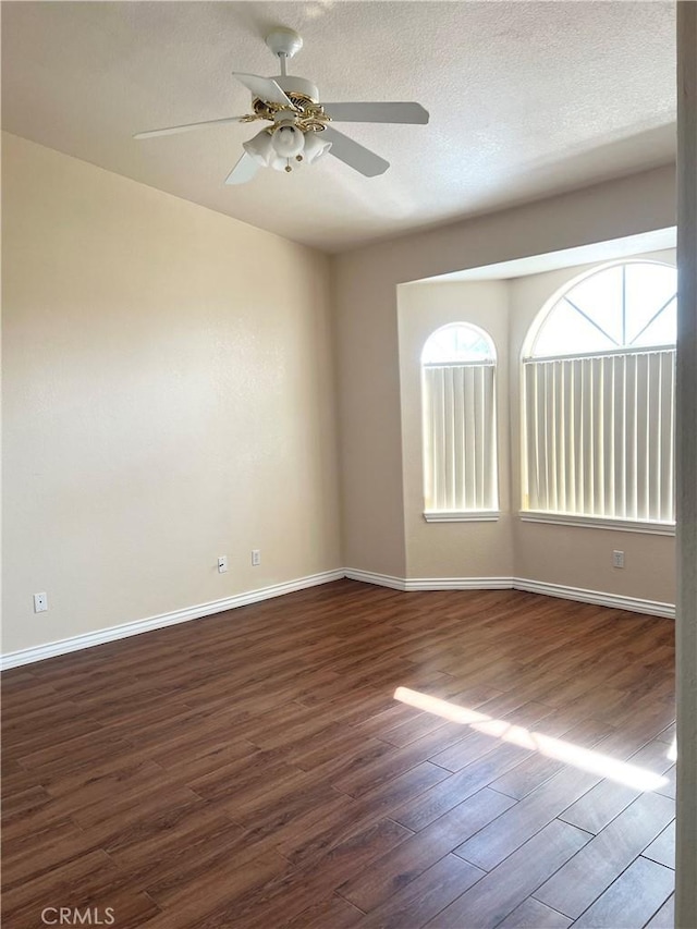 unfurnished room featuring dark wood-type flooring, ceiling fan, a textured ceiling, and baseboards