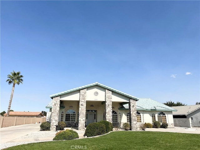 view of front facade with a front yard, stone siding, fence, and stucco siding