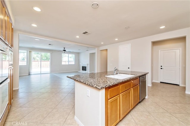 kitchen with light stone countertops, sink, ceiling fan, stainless steel dishwasher, and a kitchen island with sink