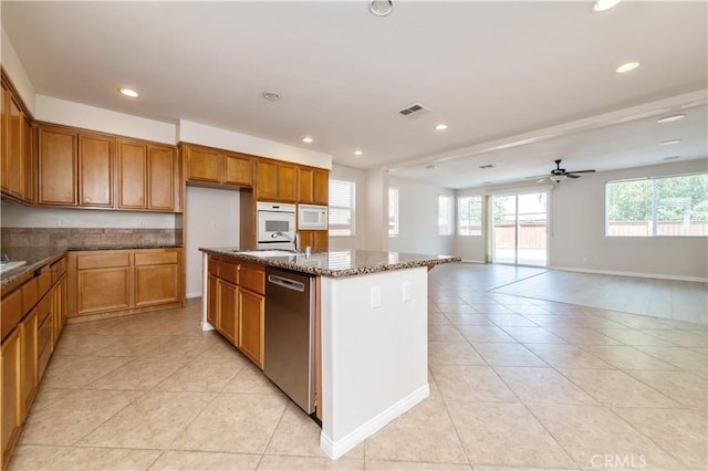 kitchen with dark stone counters, white microwave, ceiling fan, dishwasher, and a center island