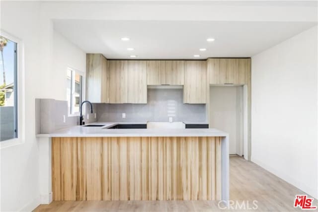 kitchen featuring light brown cabinets, backsplash, sink, light wood-type flooring, and kitchen peninsula