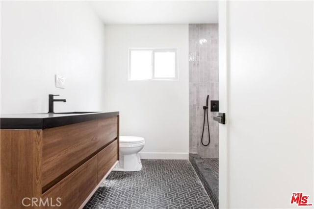 bathroom with tile patterned floors, vanity, toilet, and tiled shower