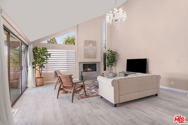 living room with high vaulted ceiling, light wood-type flooring, a fireplace, and an inviting chandelier