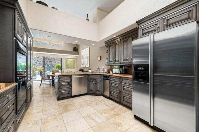 kitchen featuring stainless steel appliances, sink, a towering ceiling, kitchen peninsula, and dark brown cabinets