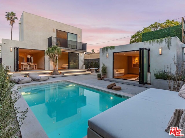 back house at dusk featuring a patio and a fenced in pool