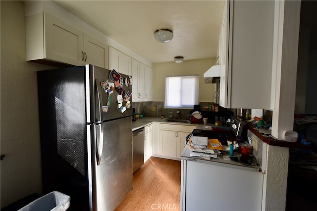 kitchen featuring white cabinets, backsplash, extractor fan, appliances with stainless steel finishes, and light wood-type flooring