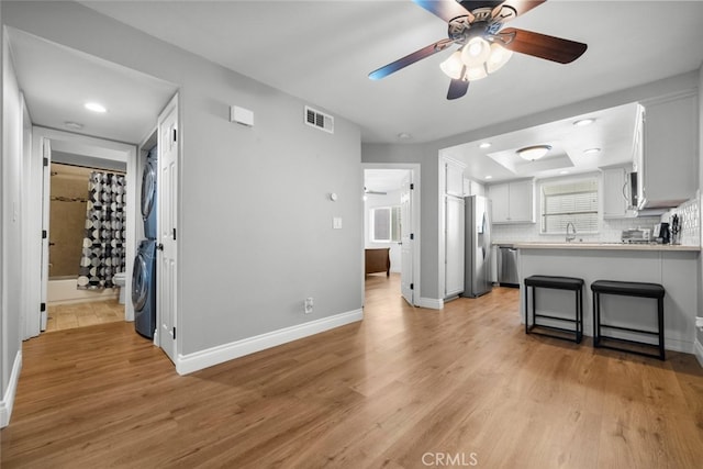 kitchen with white cabinetry, stainless steel appliances, light hardwood / wood-style flooring, kitchen peninsula, and stacked washer and dryer