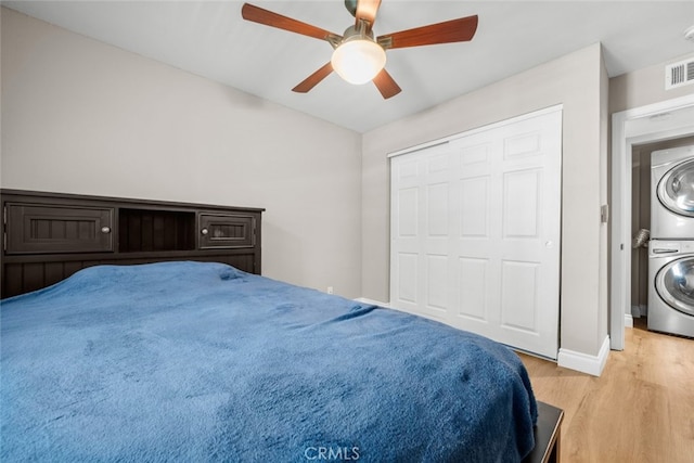 bedroom with a closet, stacked washer / dryer, ceiling fan, and light hardwood / wood-style flooring