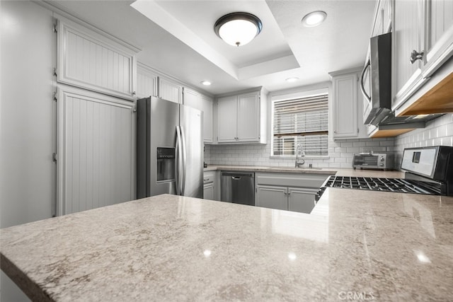 kitchen featuring kitchen peninsula, backsplash, stainless steel appliances, a raised ceiling, and sink