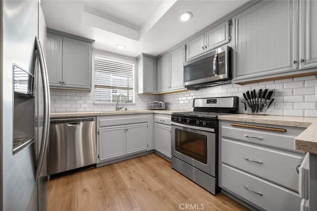 kitchen with gray cabinetry, stainless steel appliances, light hardwood / wood-style floors, and sink