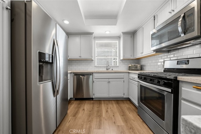 kitchen featuring white cabinets, appliances with stainless steel finishes, light hardwood / wood-style flooring, and a raised ceiling