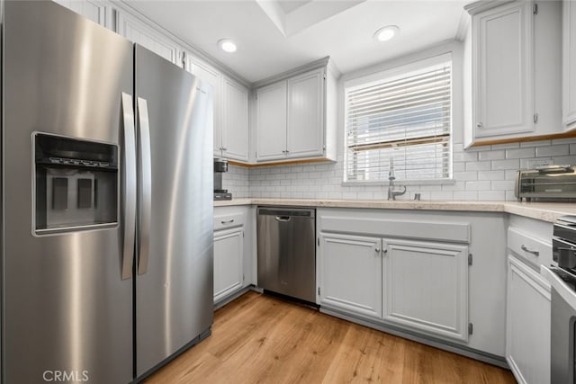 kitchen featuring sink, stainless steel appliances, light hardwood / wood-style flooring, backsplash, and white cabinets