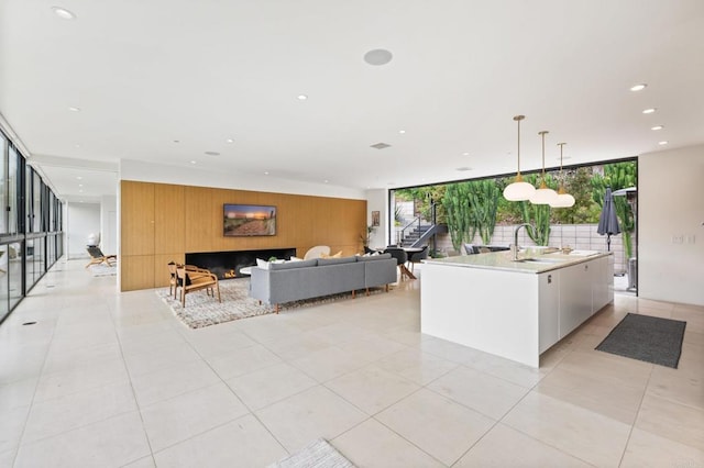 kitchen with a wall of windows, a kitchen island with sink, hanging light fixtures, and white cabinetry