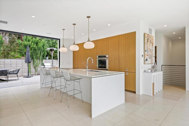 kitchen with pendant lighting, light stone counters, a large island with sink, sink, and oven