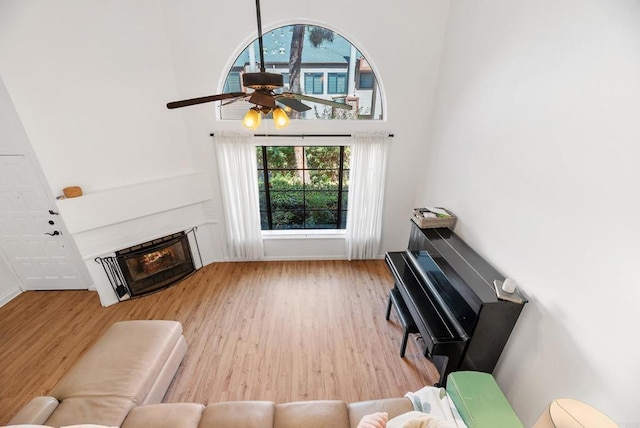 living room with ceiling fan, light hardwood / wood-style flooring, and a towering ceiling