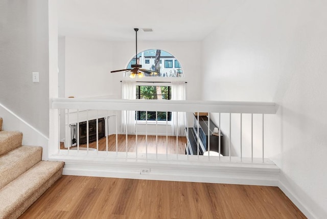 stairway with ceiling fan, a fireplace, and wood-type flooring