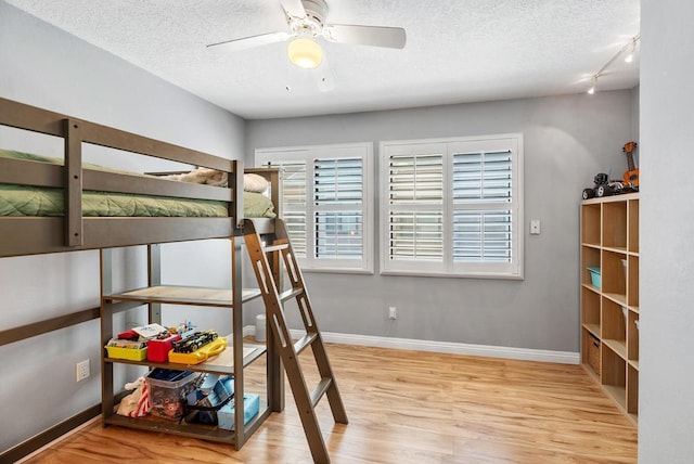 bedroom featuring light wood-type flooring, a textured ceiling, rail lighting, and ceiling fan