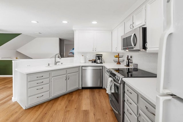 kitchen featuring white cabinetry, sink, kitchen peninsula, light hardwood / wood-style floors, and appliances with stainless steel finishes