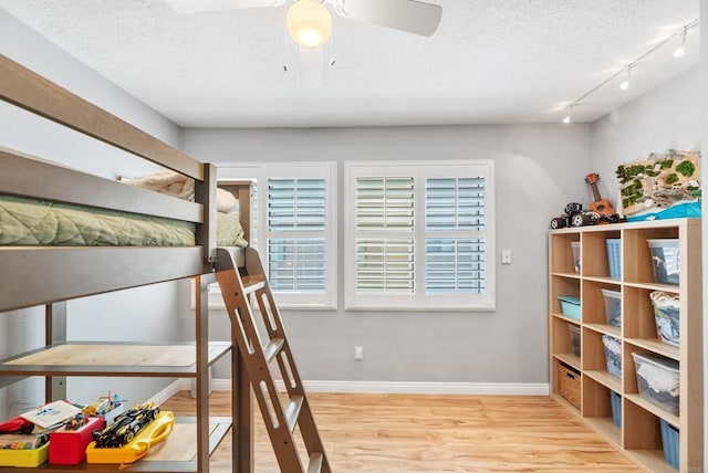 bedroom featuring ceiling fan, rail lighting, a textured ceiling, and light wood-type flooring