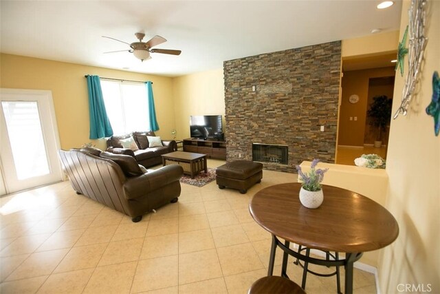 living room with ceiling fan, light tile patterned floors, and a stone fireplace