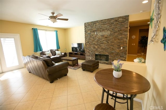 tiled living room featuring a stone fireplace and ceiling fan