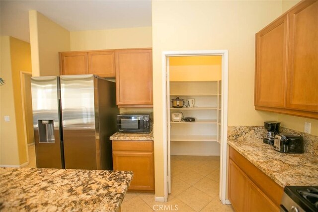 kitchen with stainless steel refrigerator with ice dispenser, light stone countertops, and light tile patterned floors