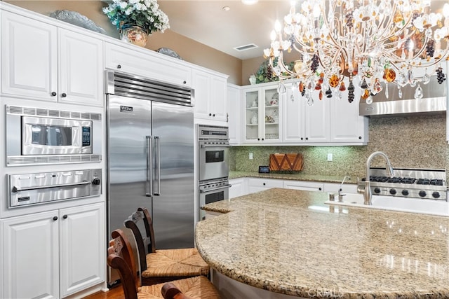 kitchen with white cabinets, built in appliances, light stone countertops, and hanging light fixtures