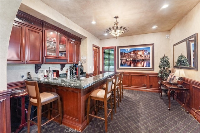 bar featuring a notable chandelier, dark stone countertops, and decorative light fixtures