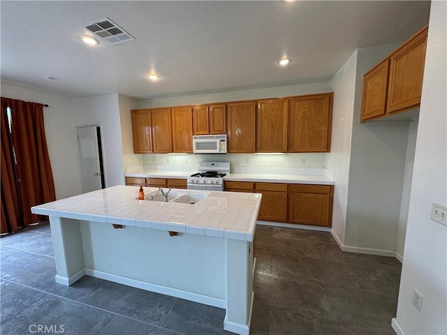 kitchen featuring white appliances, sink, an island with sink, tile counters, and a kitchen bar